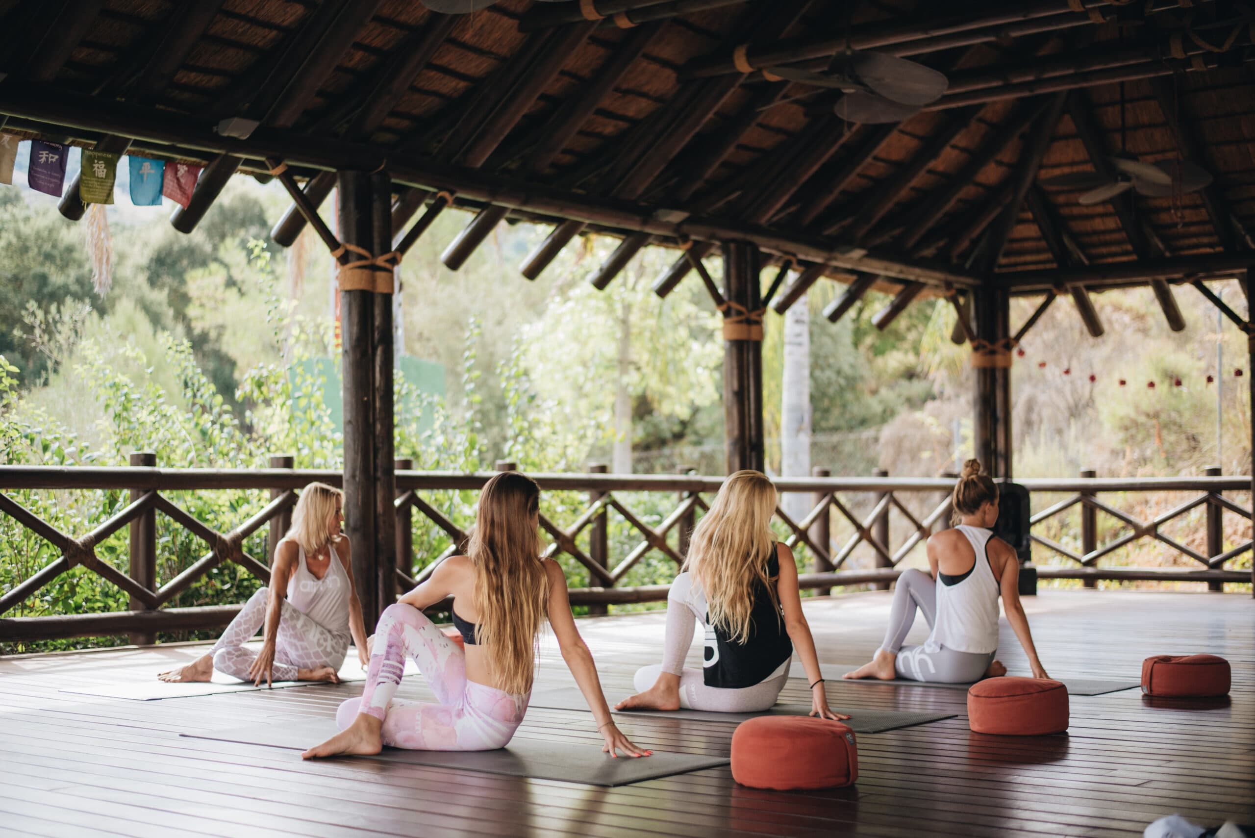 Women practicing yoga stretches in a serene wooden pavilion surrounded by lush greenery at a European yoga retreat.