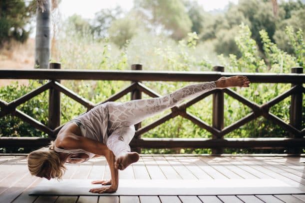 A woman practicing a challenging Pilates pose on a wooden deck surrounded by lush greenery during a Pilates retreat.